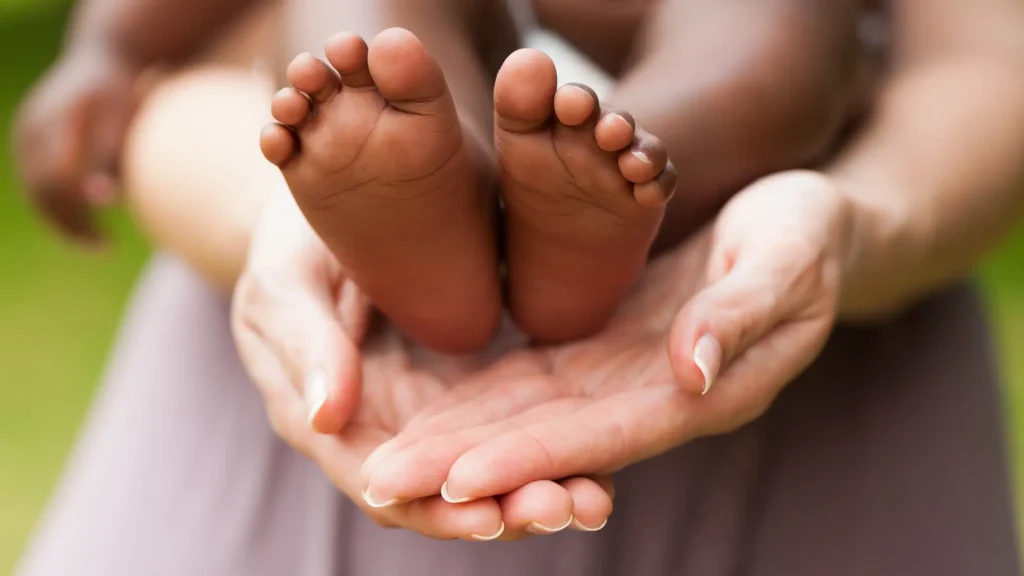 Adult hands gently holding a baby’s feet.