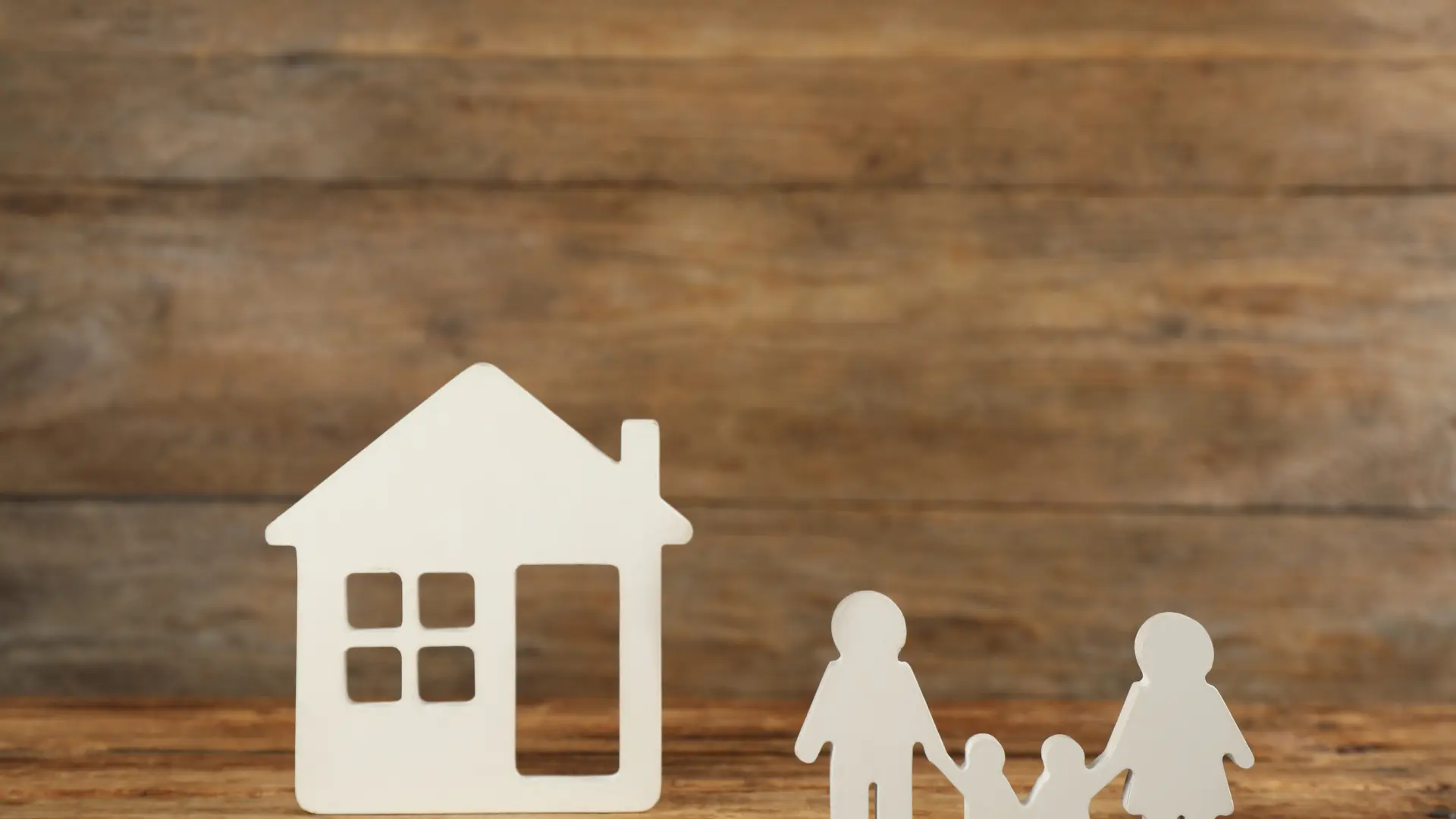 Paper cut-out of a house and family figures against a wooden background.